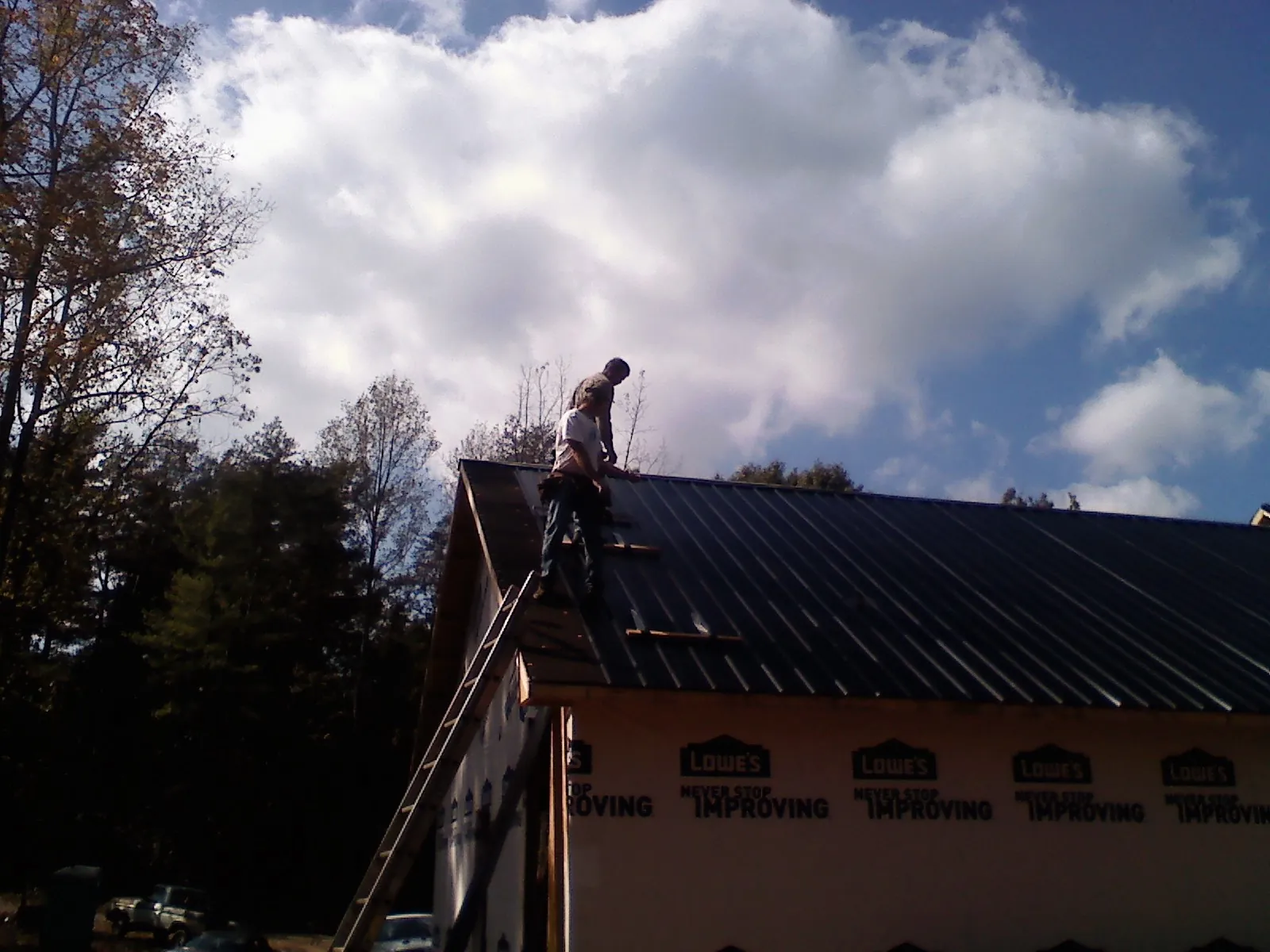 Roofer fastening dark metal panels high against a cloudy sky, from a Roof Inspection job in Albion